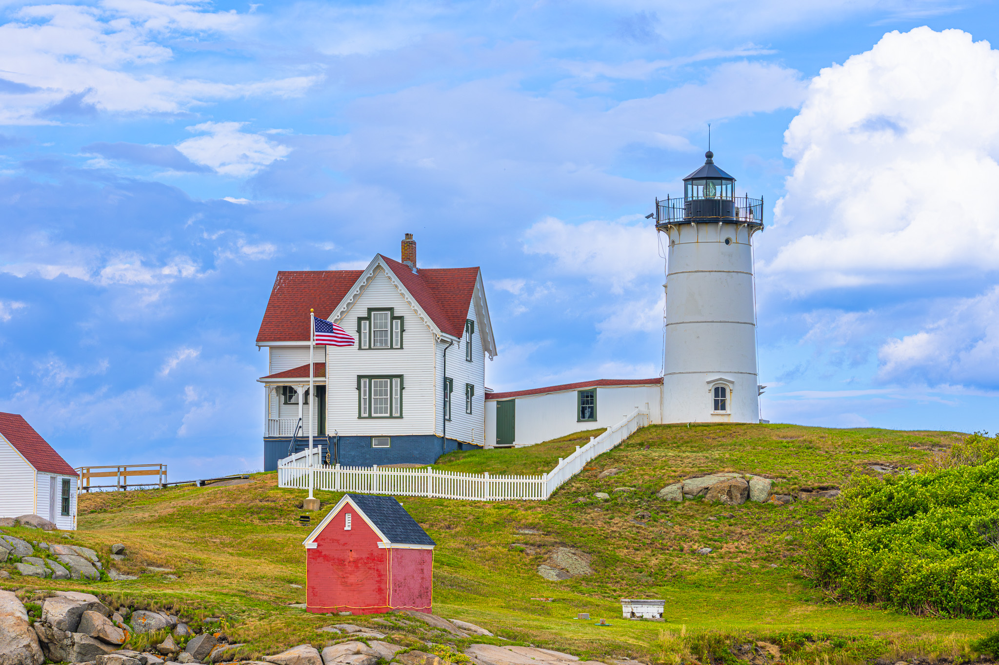 A lighthouse next to a building on an island with a blue sky behind them